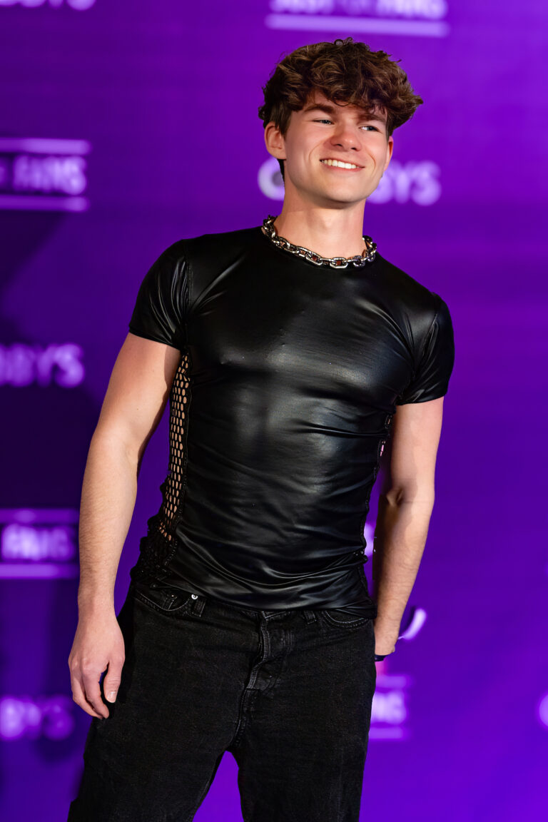 German creator Twink Frosty posing in a black wet-look shirt and steel chain necklace on the Purple Carpet at Grabbys Europe 2026 in Torremolinos.
